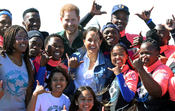 영국 해리 왕자와 메간 마클 왕자비(가운데)가 24일(현지시간) 남아프리카 케이프타운의 몬와비시 해변에서 NGO ‘Waves for Change’을 방문하는 동안 그룹 활동으로 서핑 강사 멘토들과 함께하고 있다. EPA 연합뉴스