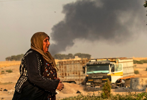 시리아의 한 여인이 9일(현지시간) 터키 국경 라스 알아인의 외곽에서 터키군의 공습으로 연기가 피어오르는 것을 배경으로 걷고 있다. 라스 알아인 AFP 연합뉴스 