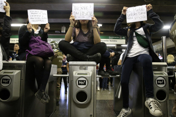 칠레 산티아고의 지하철 요금 인상에 반대하는 학생들이 지난 18일(현지시간) 한 개찰구를 막은 채 남미 유명 민중가요 제목인 ‘단결된 민중은 패배하지 않는다’ 등의 문구가 쓰인 손팻말을 들고 시위하고 있다. 산티아고 AP 연합뉴스