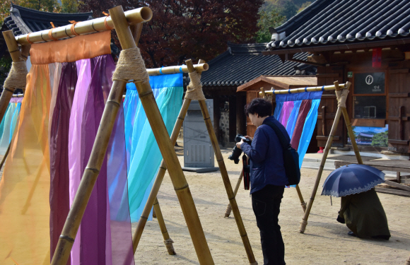 5일 서울 중구 남산골한옥마을에서 열리고 있는 ‘한옥, 걸다’ 전시에서 관람객 및 관광객들이한옥마을 마당에 펼쳐지는 ‘한복 치마’를 주제의 이승주 한복 디자이너의 전시를 배경으로 사진촬영을 하고 있다. 2019.11.5.    이종원 선임기자 jongwon@seoul.co.kr