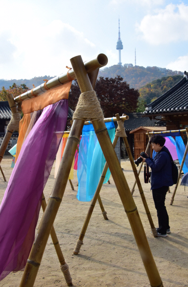 5일 서울 중구 남산골한옥마을에서 열리고 있는 ‘한옥, 걸다’ 전시에서 관람객 및 관광객들이한옥마을 마당에 펼쳐지는 ‘한복 치마’를 주제의 이승주 한복 디자이너의 전시를 배경으로 사진촬영을 하고 있다. 2019.11.5.    이종원 선임기자 jongwon@seoul.co.kr