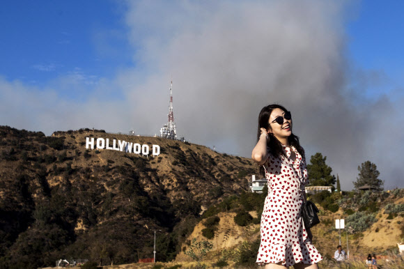 관광객들이 9일(현지시간) 미국 캘리포니아주 로스앤젤레스의 할리우드 사인 뒤에서 바햄 화재의 연기가 피어오르고 있을때, 셀카와 사진을 찍으며 즐거운 시간을 보내고 있다. 최근 언론 보도에 따르면 화재는 25에이커를 태웠고 현재는 진압되고 있다. EPA 연합뉴스