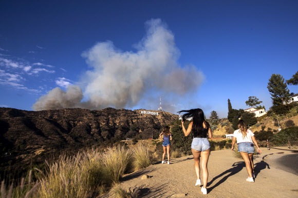 관광객들이 9일(현지시간) 미국 캘리포니아주 로스앤젤레스의 할리우드 사인 뒤에서 바햄 화재의 연기가 피어오르고 있을때, 셀카와 사진을 찍으며 즐거운 시간을 보내고 있다. 최근 언론 보도에 따르면 화재는 25에이커를 태웠고 현재는 진압되고 있다. EPA 연합뉴스