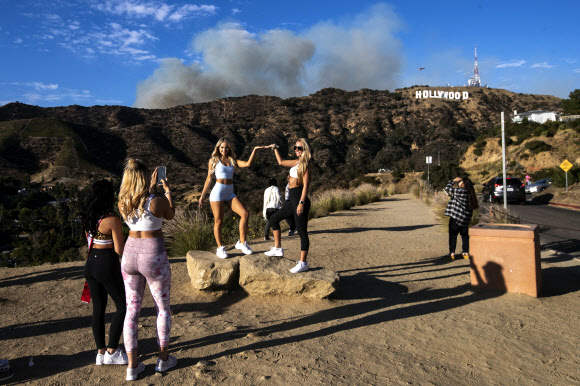 관광객들이 9일(현지시간) 미국 캘리포니아주 로스앤젤레스의 할리우드 사인 뒤에서 바햄 화재의 연기가 피어오르고 있을때, 셀카와 사진을 찍으며 즐거운 시간을 보내고 있다. 최근 언론 보도에 따르면 화재는 25에이커를 태웠고 현재는 진압되고 있다. EPA 연합뉴스