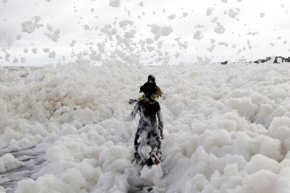 어린이가 1일(현지시간) 인도 첸나이에서 방류된 오염물질이 파도와 섞여 엄청난 거품으로 뒤덮인 벵골 만의 마리나 해변에서 놀고 있다. AP 연합뉴스
