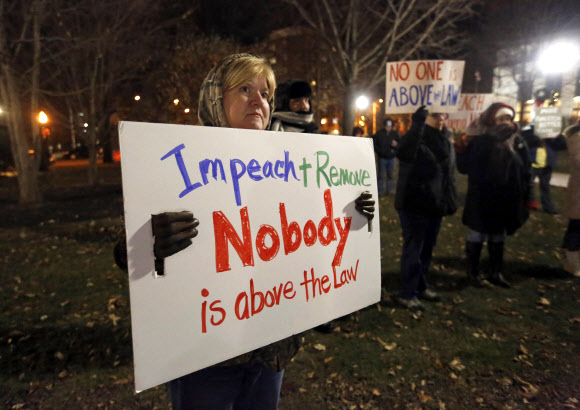 미국 여성 티나 존슨이 하원 탄핵소추안 표결을 하루 앞둔 17일(현지시간) 아이오와주 두부퀘에 있는 워싱턴 광장에서 진행된 탄핵 지지 집회 도중 “누구도 법 위에 있지 않다”는 팻말을 들고 시위를 벌이고 있다. 두부퀘 AP 연합뉴스 