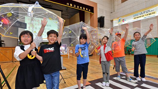 서울 고산초등학교 학생들이 현대모비스가 배포한 투명우산을 쓰고 손을 든 채 횡단보도를 건너는 연습을 하고 있다.  현대모비스 제공