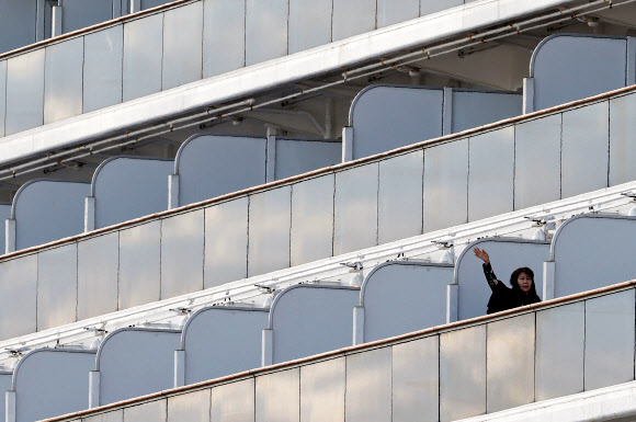7일(현지시간) 일본 요코하마 다이코쿠 피어 크루즈 터미널에 정박해 있는 대형 크루즈선 ‘다이아몬드 프린세스’호의 승객들이 마스크를 쓰고 손을 흔들고 있다. 로이터 연합뉴스