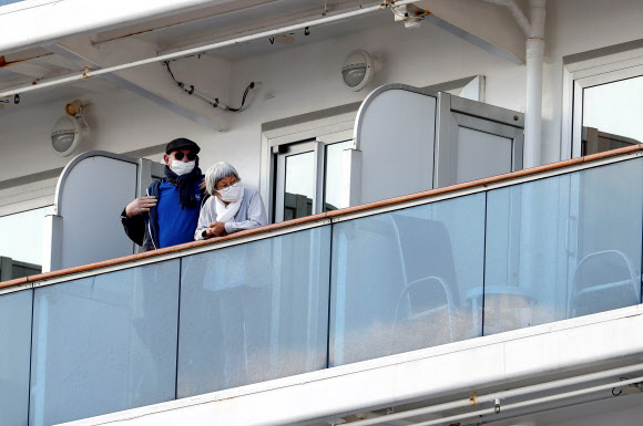 7일(현지시간) 일본 요코하마 다이코쿠 피어 크루즈 터미널에 정박해 있는 대형 크루즈선 ‘다이아몬드 프린세스’호의 승객들이 마스크를 쓰고 나와 있다. 로이터 연합뉴스