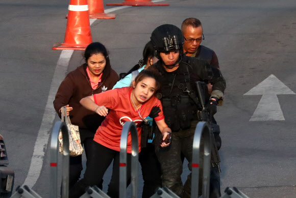 A woman is assisted by Thai security forces evacuating people stranded inside the Terminal 21 shopping mall following a gun battle, to try to stop a soldier on a rampage after a mass shooting, Nakhon