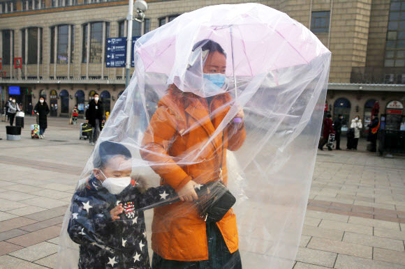 한 여성이 11일(현지시간) 중국 베이징 기차역에서 코로나바이러스로부터 자신과 아이를 보호하기 위해 마스크를 쓰고 우산에 비닐을 씌워 이동하고 있다. EPA 연합뉴스
