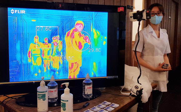 중국 우한(武漢)에서 시작된 신종 코로나바이러스 감염증(코로나 19)이 국제적으로 빠르게 확산하는 16일 오후 베트남 하노이 경남 랜드마크타워(랜드마크72) 한식당 식객에서 마스크와 일회용 앞치마를 착용한 직원이 열화상 카메라를 통해 발열을 비접촉 원적외선으로 점검하고 있다.    베트남 한식당 ‘식객 하노이’와 ‘식객 푸꾸옥’은 입구에 열화상 카메라를 설치 운영하고 있다. 고열로 의심되는 손님은 일대일 비접촉 발열 검사 후 체온이 38.5도 이상이면 입장이 금지된다. 박찬호 식객 대표는 “이곳은 하노이에서 가장 높은 빌딩에 위치해 각종 오염에 비교적 청정구역으로 알려졌지만 베트남 주재원과 정부 관계자들이 주 고객인 만큼 위생과 안전에 매우 민감하다. 방역의 관점에서 위험을 최소화하기 위해 직원들은 항상 마스크를 착용하고 주기적으로 손을 씻은 뒤 소독하며, 영업시간이 끝나면 전 구역에 분무식 소독제를 뿌리고 자외선램프로 공기 중 살균을 하고 있다. 모든 고객을 위해 손 세정제와 일회용 소독제와 앞치마를 제공하는 등 ‘코로나 19’ 감염 예방에 최선을 다하고 있다”고 말했다. 2020.2.16 독자 제공