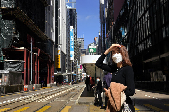 홍콩의 한 여성이 마스크를 쓴 채 길을 건너려 교차로에 서 있다. 홍콩에서는 지난해 하반기부터 어이진 민주화 시위로 경제가 엉망이 된 데다 코로나19 확산마저 겹쳐 거리가 텅 비어 있다. 홍콩 AP 연합뉴스 