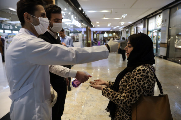 코로나19 확산 사태를 겪고 있는 이란 테헤란의 한 쇼핑센터에서 검역 직원들이 한 여성의 체온을 측정하며 손소독제를 뿌리고 있다. 테헤란 AP 연합뉴스
