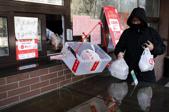 중국에서 코로나19가 한창 기승을 부리던 지난달 23일 베이징의 한 상점에서 코로나19 바이러스의 접촉을 막기 위해 큰 박스 속에 담아 내준 식료품 꾸러미를 모자로 입을 가린 고객이 꺼내가는 모습. 베이징 AP 연합뉴스
