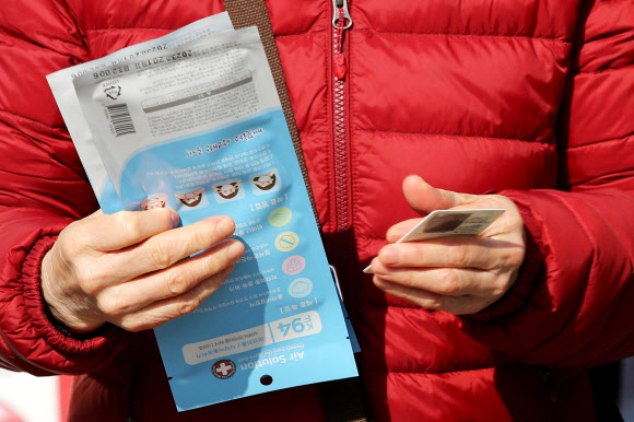 6일 오전 서울 종로5가 인근의 한 약국을 찾은 한 시민이 구매한 마스크와 신분증을 들고 있다.  다음 주부터는 약국·우체국·농협에 마스크 중복구매 확인시스템을 구축해 마스크 판매자가 구매자의 신분증을 확인하고, 구매 이력을 체크해 1인당 1주(월~일요일)당 2매만 살 수 있도록 할 계획이다. 2020.3.6  연합뉴스