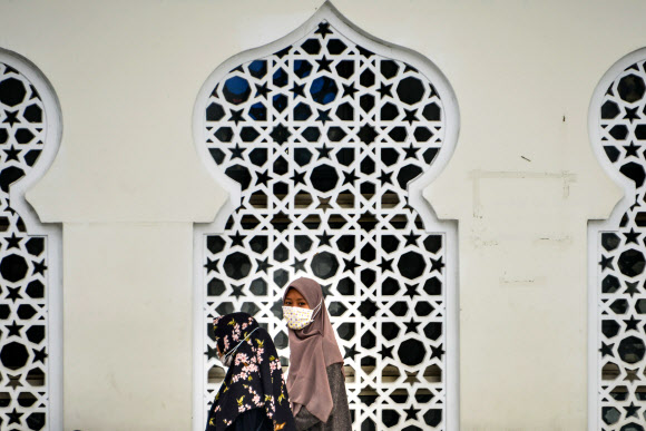 6일 인도네시아 아체주의 주도 반다아체의 바이투라만 그랜드 모스크 앞에서 마스크를 쓴 무슬림 여성들이 근심스러운 표정으로 걸어가고 있다. 인도네시아는 지난 2일 64세의 여성과 31세의 딸이 코로나19 양성반응을 보이면서 전국이 공포에 휩싸였다. 반다이체 AFP 연합뉴스