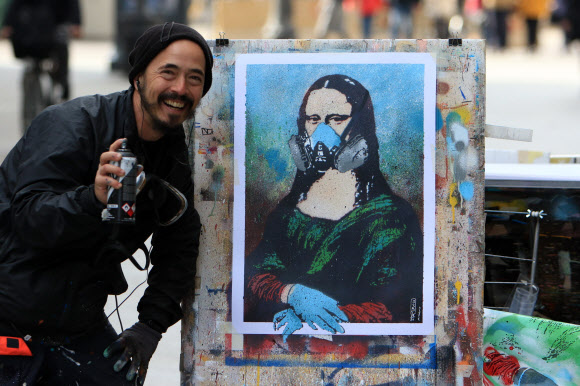 이탈리아의 거리 예술가 세르지오 로시가 6일(현지시간) 북부 밀라노의 한 거리에서 레오나르도 다빈치의 모나리자 주인공에게 화생방 마스크와 수술용 장갑을 착용시킨 패러디 작품 ‘병든 사회’를 선보이고 있다. 밀라노 EPA 연합뉴스 