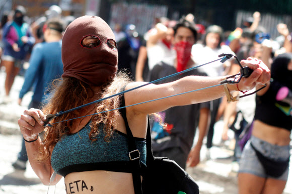 ‘세계 여성의 날’인 8일(현지시간) 칠레 산티아고에서 열린 대규모 집회에서 참가자가 시위중 새총을 쏘고 있다. 로이터 연합뉴스