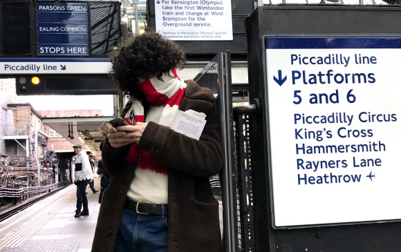 13일 영국 런던의 한 지하철역 승강장에서 한 남자가 축구 응원 스카프로 얼굴을 동여맨 채 핸드폰을 들여다 보고 있다. 잉글랜드 프리미어리그를 비롯한 유럽 5대 축구리그는 지난 주말 경기를 앞두고 코로나19 확산을 이유로 리그를 모두 중단했다.AP 연합뉴스