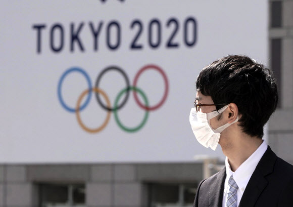마스크를 쓴 일본의 한 직장인이 18일 2020 도쿄올림픽 엠블럼이 그려진 간판 옆을 지나가고 있다. 2020.3.18 EPA 연합뉴스