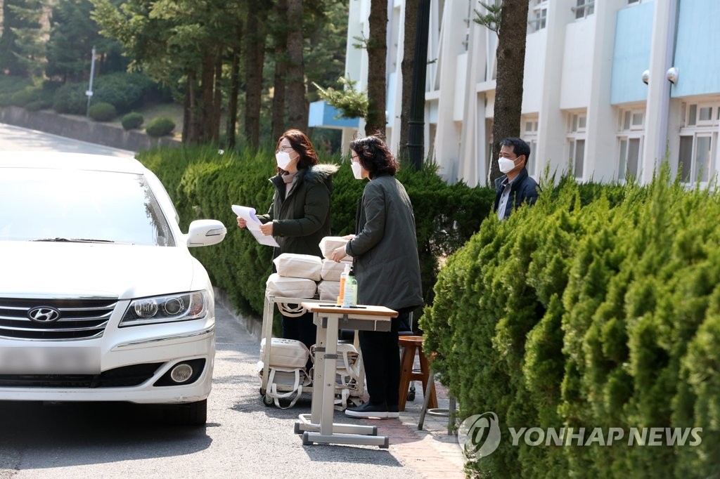 19일 경북 포항제철중학교에서 교사가 차를 타고 온 신입생 학부모에게 교과서를 나눠주고 있다. 연합뉴스