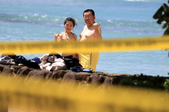 사람들이 20일(현지시간) 미국 하와이주 호놀룰루의 노란색 경고 테이프로 둘러싸인 와이키키 해변에서 사진을 찍고 있다. 호놀룰루는 코로나바이러스의 확산을 막기 위해 모든 공원과 휴양지를 폐쇄했다. AP 연합뉴스