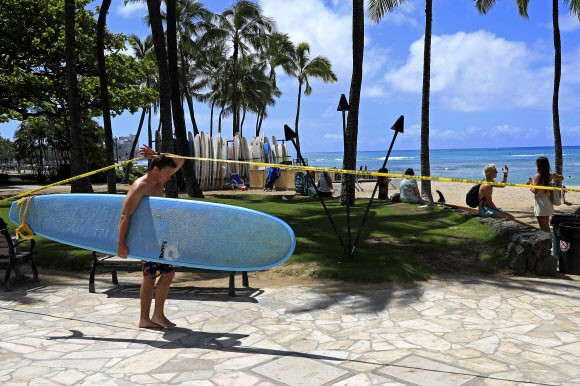 서퍼가 20일(현지시간) 미국 하와이주 호놀룰루의 노란색 경고 테이프로 둘러싸인 와이키키 해변에 들어가고 있다. 호놀룰루는 코로나바이러스의 확산을 막기 위해 모든 공원과 휴양지를 폐쇄했다. AP 연합뉴스