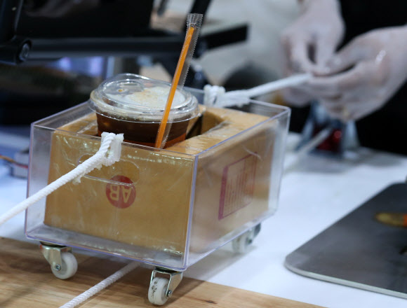 직원이 21일(현지시간) 태국 방콕의 카세타트 대학 내 커피숍에서 사람들 사이의 사회적 거리를 보장하기 위해 도르래 시스템을 사용해 음료를 전달하고 있다. EPA 연합뉴스