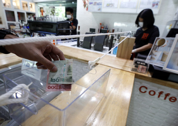 직원이 21일(현지시간) 태국 방콕의 카세타트 대학 내 커피숍에서 사람들 사이의 사회적 거리를 보장하기 위해 도르래 시스템을 사용해 음료 값을 전달받고 있다. EPA 연합뉴스