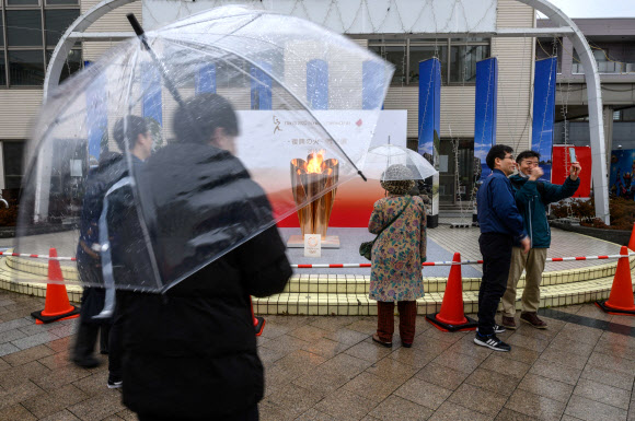 22일(현지시간) 일본 이와테현 미야코 철도역 밖에 전시된 ‘2020 도쿄 올림픽’ 성화 앞에서 마스크를 쓴 시민들이 기념촬영을 하고 있다. AFP 연합뉴스