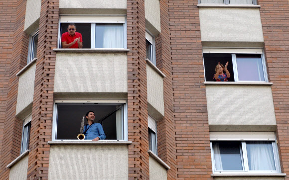 스페인 북부 아스투리아스 히혼에 사는 색소폰 연주자 미구엘 갈레고가 봉쇄령이 15일 연장돼 바깥 출입을 못해 갑갑해 하는 이웃들에게 연주를 들려주자 주민들이 갈채로 답하고 있다. 　히혼 EPA 연합뉴스