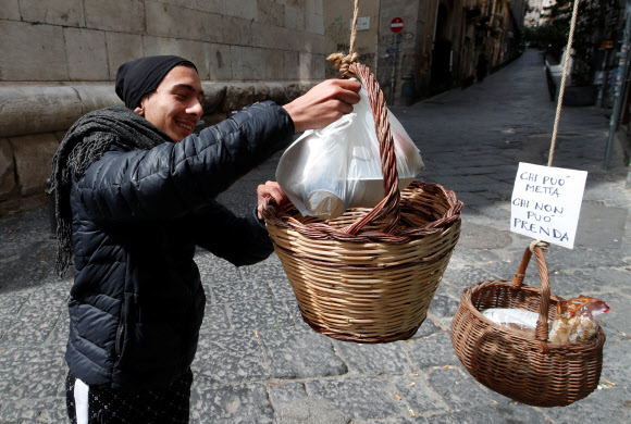 이탈리아 나폴리의 한 남성이 30일(현지시간) 음식이나 생필품을 기부할 수 있다는 팻말이 붙은 바구니 안에 물품을 넣어주고 있다.  나폴리 로이터 연합뉴스
