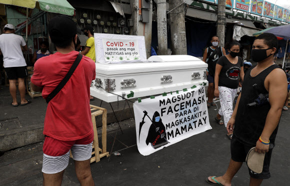 지난 9일 필리핀 마닐라의 한 시장 밖에 전시된 ‘얼굴 마스크를 쓰고 아프지 않게 하여라’는 밑단 현수막이 걸린 빈 관을 지나던 시민들이 바라보고 있다. 마닐라 AP 연합뉴스