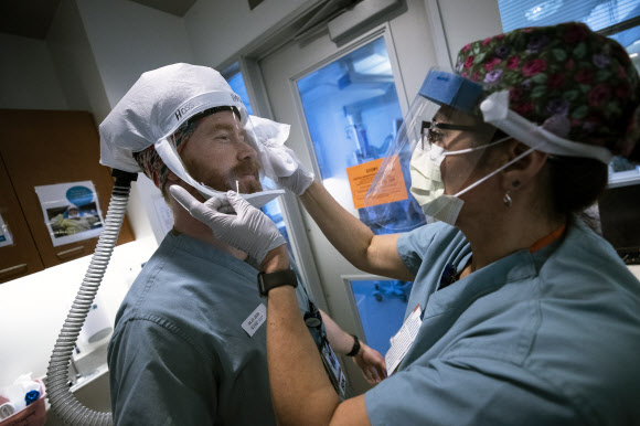   미국 캘리포니아주 샌디에이고의 샤프 그로스몬트 병원 간호사 실비아 로모(오른쪽)가 22일(현지시간) 집중치료 병상에 들어가는 호스 리처슨의 마스크를 소독해주고 있다. 샌디에이고 EPA 연합뉴스 