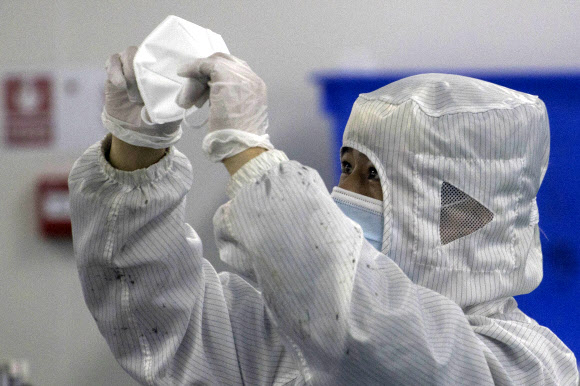 지난 12일 중국 후베이성 우한존센메디컬의 마스크용 청정실 생산라인에서 한 직원이 생산된 마스크를 면밀히 살펴보고 있다. 우한 AP 연합뉴스