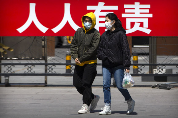 21일 중국 베이징의 한 공공공원에서 질병 확산을 통제하는 것은 모두의 책임’이라고 적힌 플래카드 앞을 남녀가 얘기를 나누며 지나가고 있다. 베이징 AP 연합뉴스