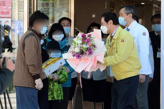 이용섭(오른쪽 노란색 옷) 광주시장이 지난달 11일 빛고을전남대병원에서 첫퇴원하는 대구의 일가족에게 축하의 꽃다발을 건네고 있다.