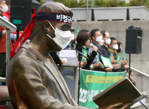 1일 오전 서울 세종문화회관 계단 앞에서 ‘2020 메이데이 민주노총 선언 기자회견’이 열리는 중 옆에 설치된 책을 읽는 동상에 비정규직 철폐 머리띠와 마스크가 씌워져 있다. 연합뉴스