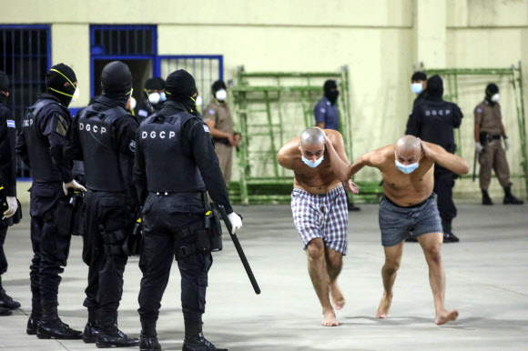 In this photo released by El Salvador Presidency Press Office police wearing masks as precautions against the new coronavirus guard inmates, also wearing masks, during a security operation after President Nayib Bukele decreed maximum emergency in prisons housing gang members at the Izalco prison in San Salvador, El Salvador, Saturday, April 25, 2020. Bukele ordered the emergency the day after more than twenty people were killed throughout country that authorities said were ordered from prisons. AP 연합뉴스