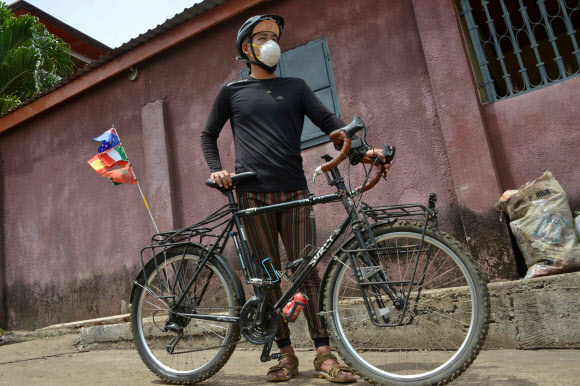 자전거로 세계일주 중인 레이몬드 리가 지난 30일 아프리카 기니의 거리에서 자전거와 함께 서 있다. 연합뉴스.