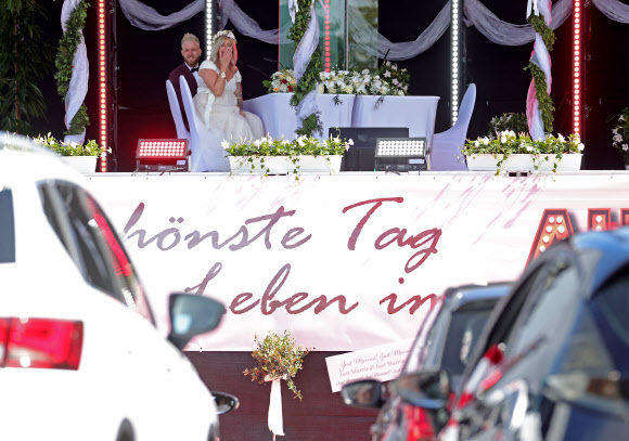 커플 제닌과 필립 스콜즈가 5일(현지시간) 독일 듀셀도르프의 드라이브인 극장에서 결혼식을 하고 있다. 코로나바이러스 대유행때문에 등록사무소의 결혼식으로 제한되어 있어, 모든 친척들과 친구들이 차에 참석할 수 있도록 드라이브인 극장의 무대에서 공식 결혼을 등록하기 시작했다.EPA 연합뉴스