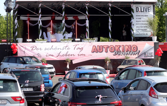 커플 제닌과 필립 스콜즈가 5일(현지시간) 독일 듀셀도르프의 드라이브인 극장에서 결혼식을 하고 있다. 코로나바이러스 대유행때문에 등록사무소의 결혼식으로 제한되어 있어, 모든 친척들과 친구들이 차에 참석할 수 있도록 드라이브인 극장의 무대에서 공식 결혼을 등록하기 시작했다.EPA 연합뉴스