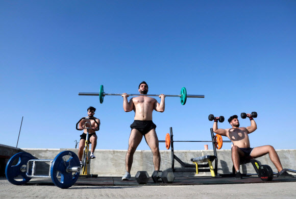 팔레스타인 보디빌딩 트레이너 무하마드 자프레(가운데)가 10일(현지시간) 웨스트 뱅크 도시 헤브론의 북서쪽에 있는 타르 쿠미야 마을의 코로나19 폐쇄로 체육관이 폐쇄됨에 따라, 학생들과 함께 건물 옥상에서 훈련을 하고 있다. AFP 연합뉴스