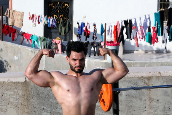 팔레스타인 보디빌딩 트레이너 무하마드 자프레가 10일(현지시간) 웨스트 뱅크 도시 헤브론의 북서쪽에 있는 타르 쿠미야 마을의 코로나19 폐쇄로 체육관이 폐쇄됨에 따라, 학생들과 함께 건물 옥상에서 훈련을 하며 포즈를 취하고 있다. AFP 연합뉴스