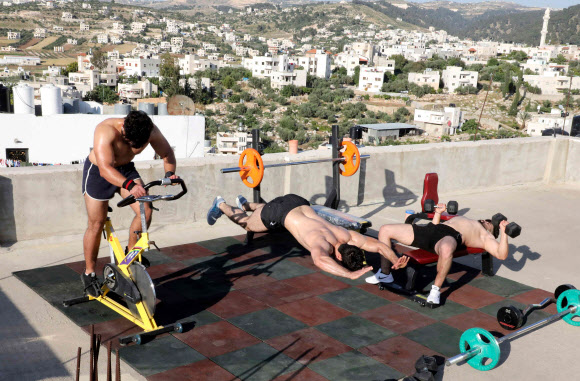 팔레스타인 보디빌딩 트레이너 무하마드 자프레(가운데)가 10일(현지시간) 웨스트 뱅크 도시 헤브론의 북서쪽에 있는 타르 쿠미야 마을의 코로나19 폐쇄로 체육관이 폐쇄됨에 따라, 학생들과 함께 건물 옥상에서 훈련을 하고 있다. AFP 연합뉴스