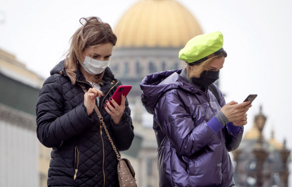 12일 코로나19 감염자 규모에서 세계 두 번째로 올라선 러시아 제2 도시인 상트페테르부르크 번화가에서 전날 마스크를 쓴 여성들이 스마트폰을 들여다보고 있다. 상트페테르부르크 AP 연합뉴스 