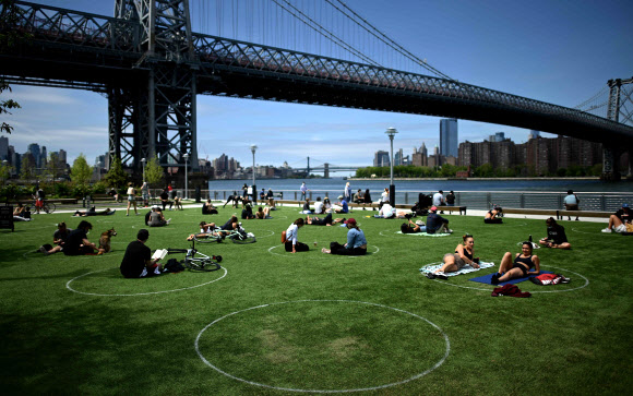 신종 코로나바이러스 감염증(코로나19)의 세계적인 확산이 이어지고 있는 가운데 17일(현지시간) 미국 뉴욕주 브루클린 인근 윌리엄스버그의 도미노 공원에서 사회적 거리두기를 위해 표시해둔 원안에 사람들이 자리를 잡고 앉아 여유를 즐기고 있다. AFP 연합뉴스