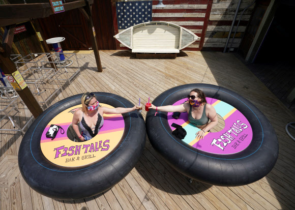 볼티모어의 트레이시 샌드리지와 줄리 브라운이 23일(현지시간) 미국 메릴랜드주 오션시티에서 피시 테일즈 바 앤 그릴이 코로나19 사회적 거리를 위해  ‘범퍼 테이블’을 고안해 재개장 해, 건배를 하며 포즈를 취하고 있다. 로이터 연합뉴스