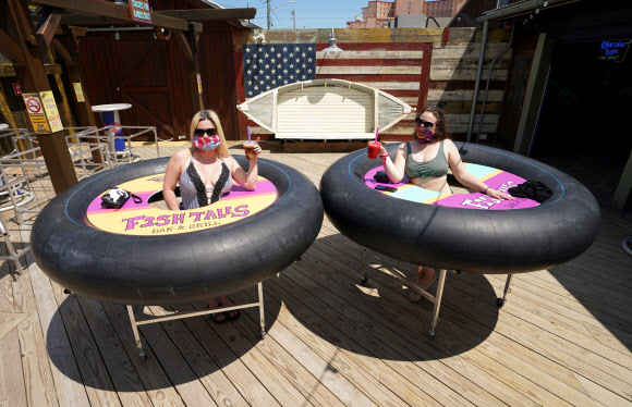 볼티모어의 트레이시 샌드리지와 줄리 브라운이 23일(현지시간) 미국 메릴랜드주 오션시티에서 피시 테일즈 바 앤 그릴이 코로나19 사회적 거리를 위해  ‘범퍼 테이블’을 고안해 재개장 해, 건배를 하며 포즈를 취하고 있다. 로이터 연합뉴스